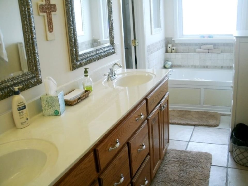 Before photo of a bathroom vanity area with older wall color, mirror, tub, and natural light