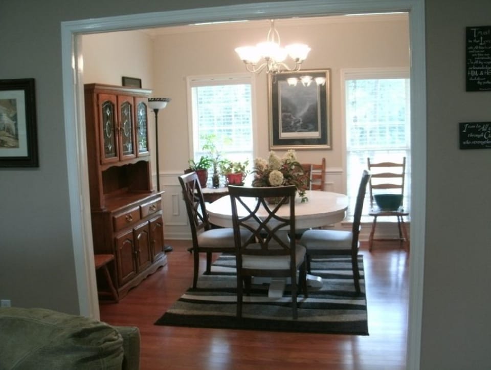 Before photo of a dining room with older wall color, wood flooring, and view through a wide doorway