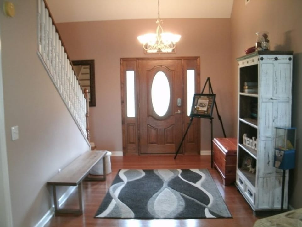 Before photo of an interior entry area with older wall color, wood door, staircase, and flooring